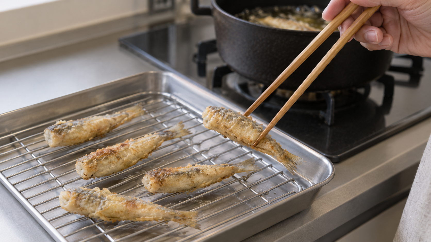 ハゼの唐揚げを菜箸で油切り網へ移す手元