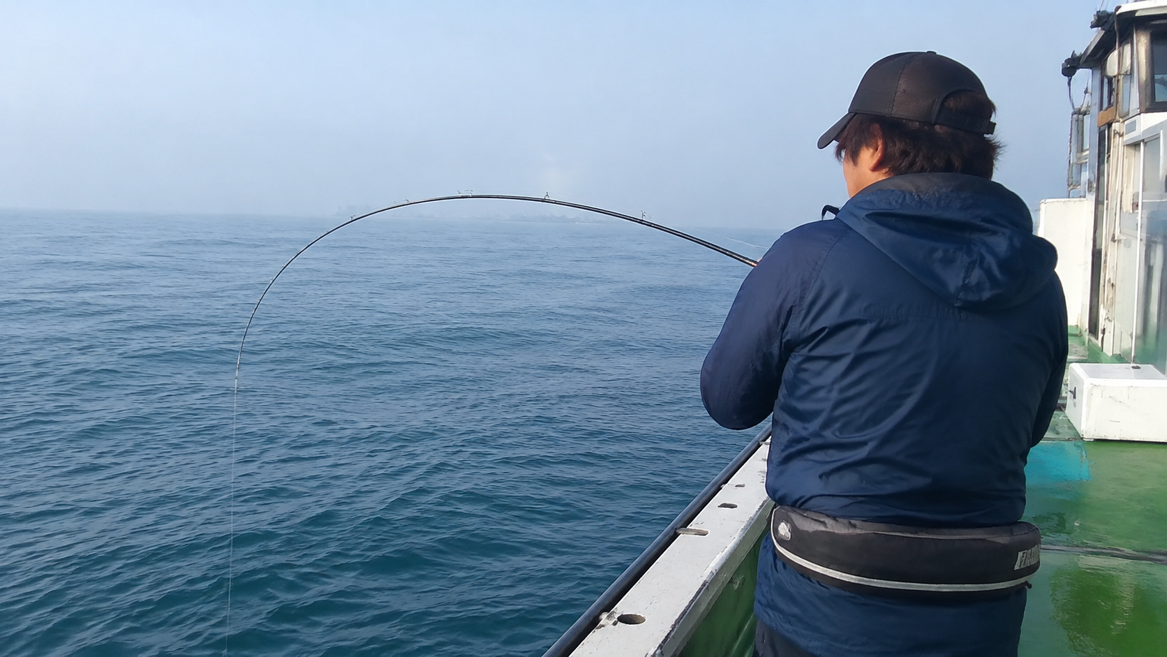 船べりで海へ向かい、しなったヒラメ竿を構える釣り人の後ろ姿
